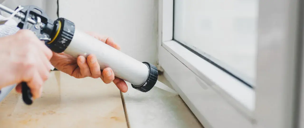 Applicazione di silicone per come isolare finestre vecchie in alluminio. Sigillatura del telaio per migliorare l'efficienza energetica.
