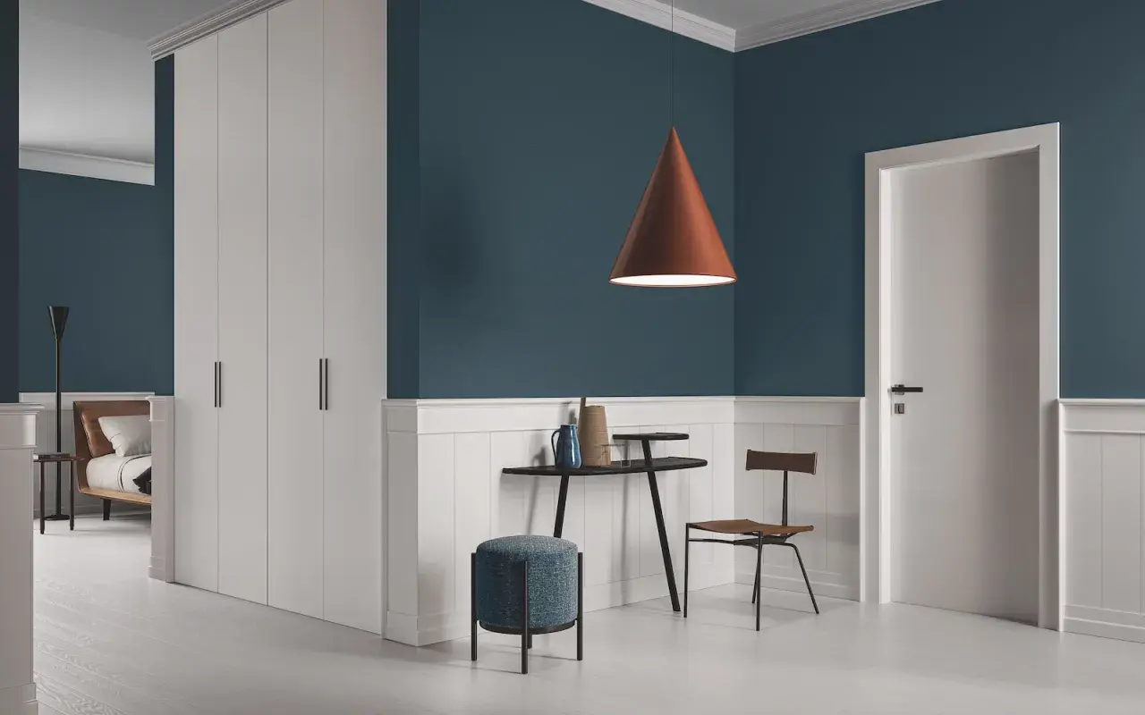 Un soggiorno moderno con pareti blu intenso e battiscopa bianco. Un lampadario color terra e infissi marroni creano un contrasto caldo.