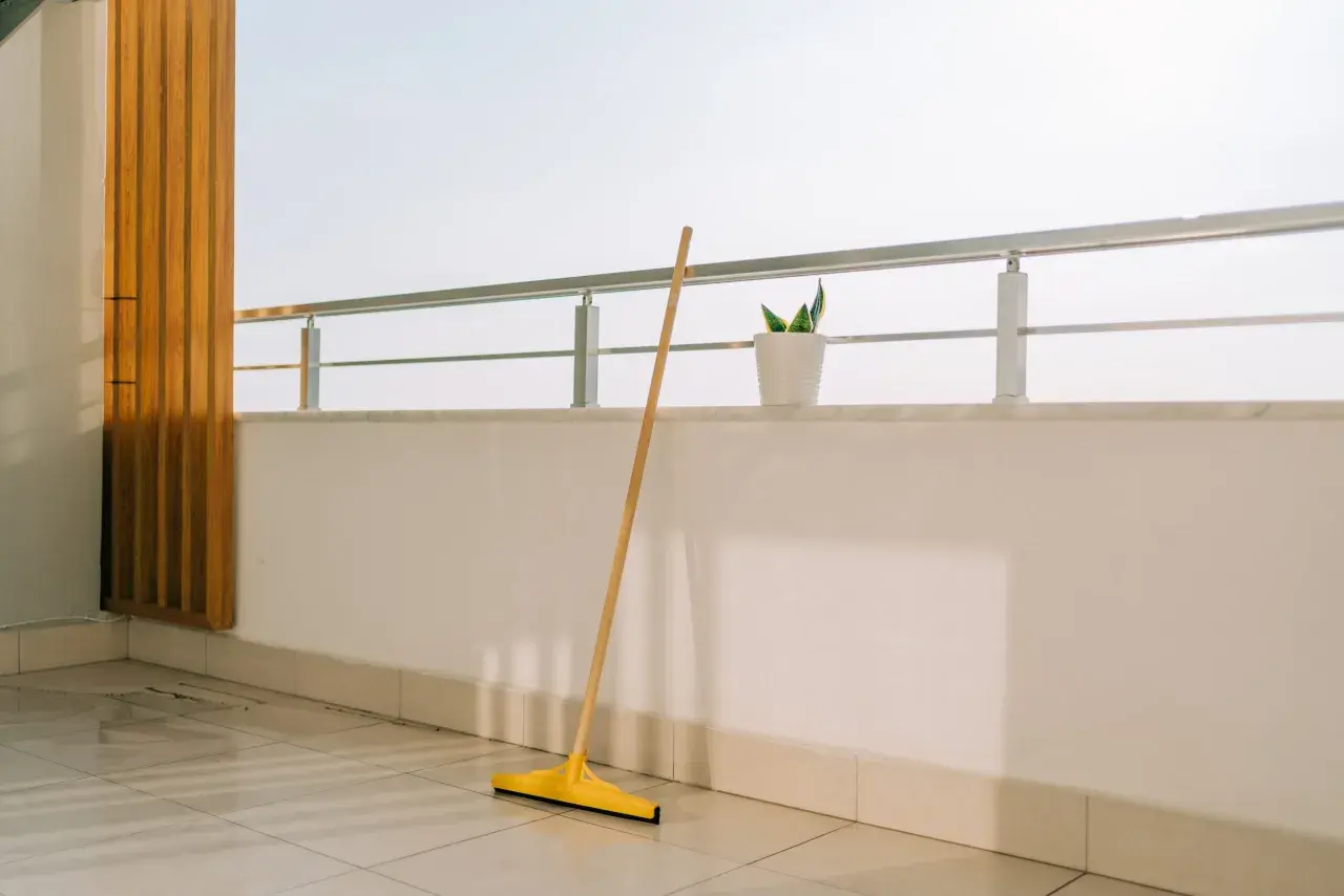 Scopa gialla appoggiata sul pavimento piastrellato, pronta per pulire la veranda del balcone.