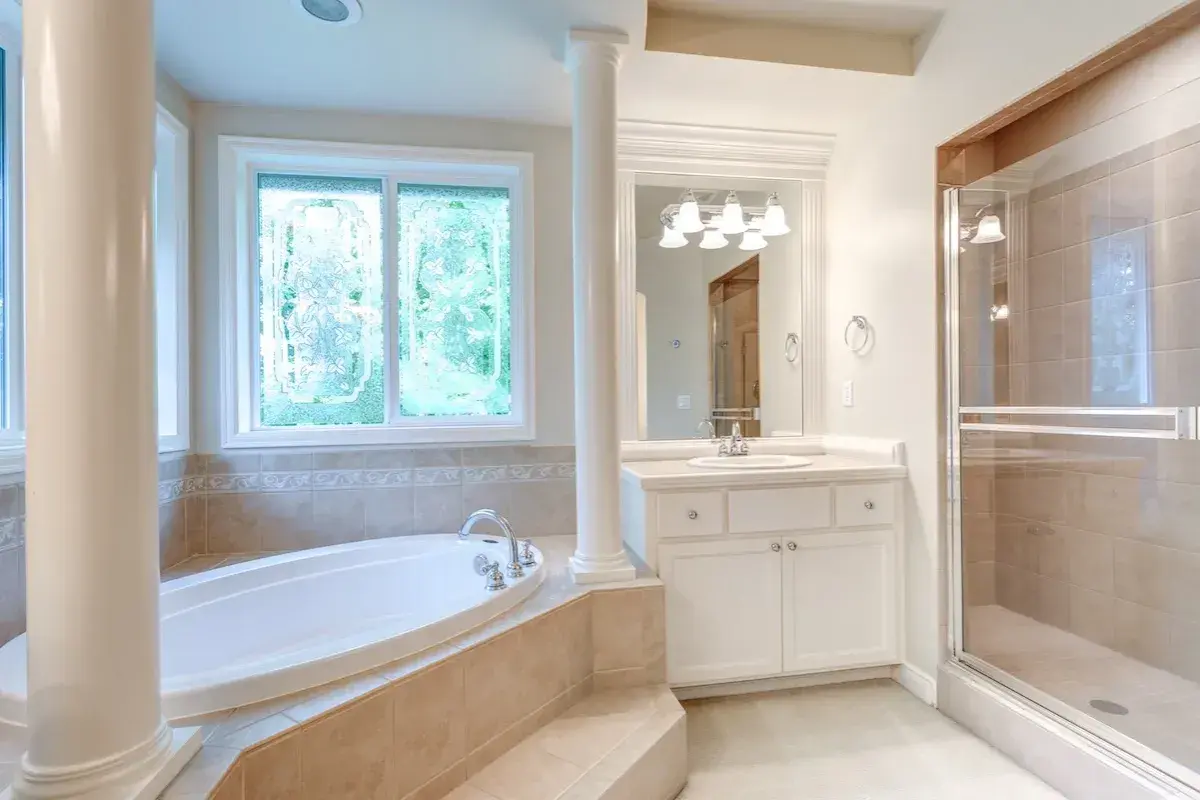 Ampia vasca da bagno sotto una finestra con vetri decorati, un bagno spazioso con doccia e lavandino.