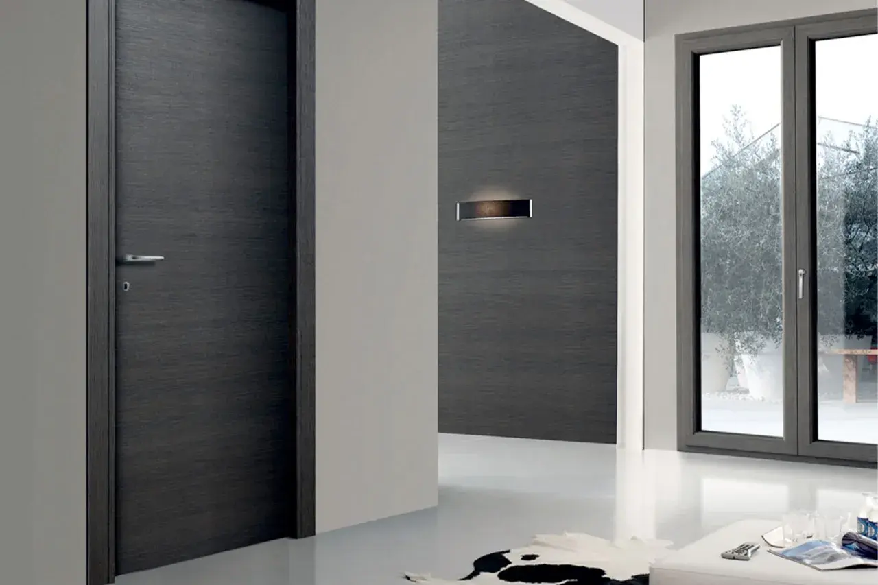Porta moderna in legno scuro e finestra con infisso grigio. La trasmittanza termica, unità di misura fondamentale per l'efficienza energetica, è un valore da considerare.