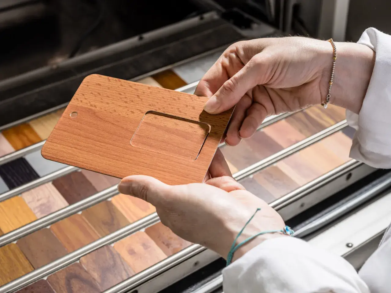Mani che esaminano un campione di alluminio color legno, con una vasta gamma di finiture lignee in esposizione.