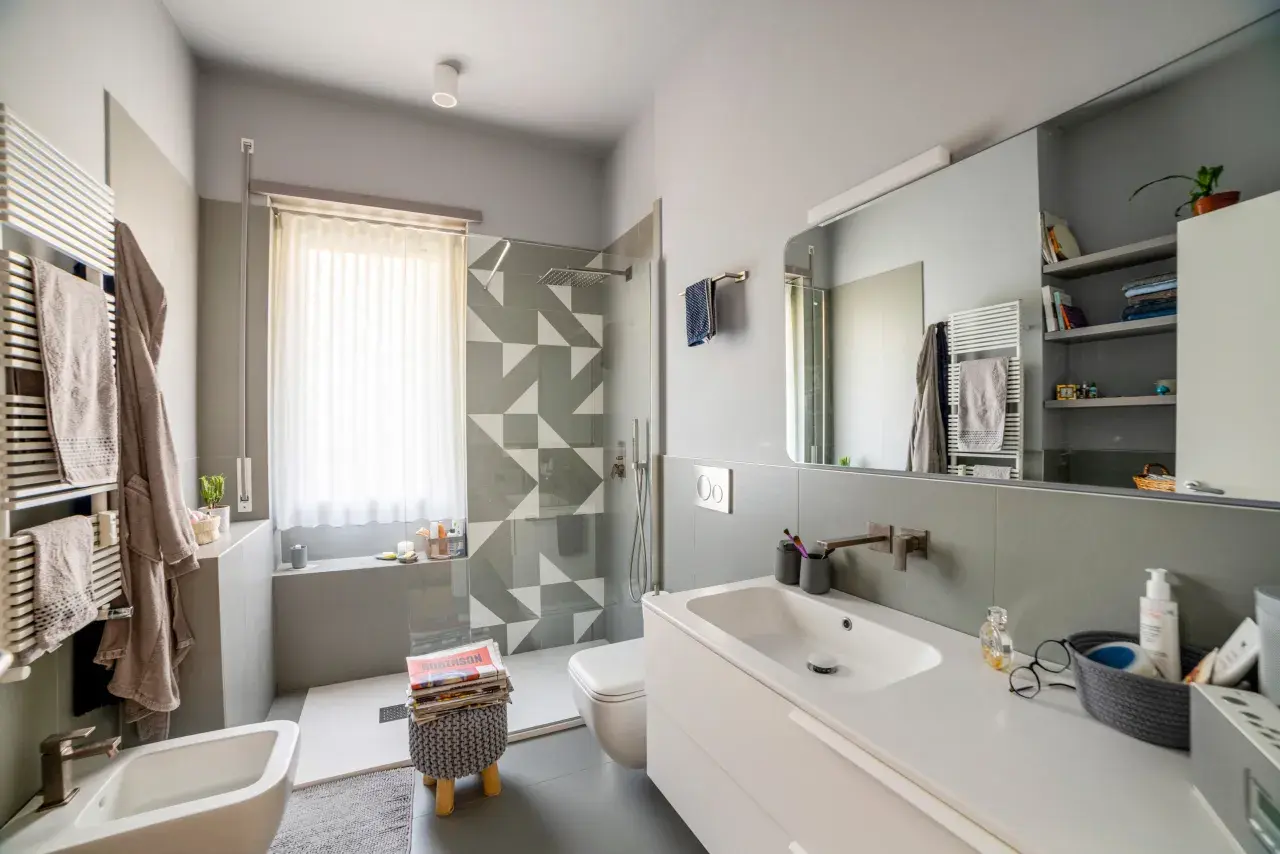 Bagno moderno con doccia su finestra, lavabo, bidet e scalda-asciugamani.