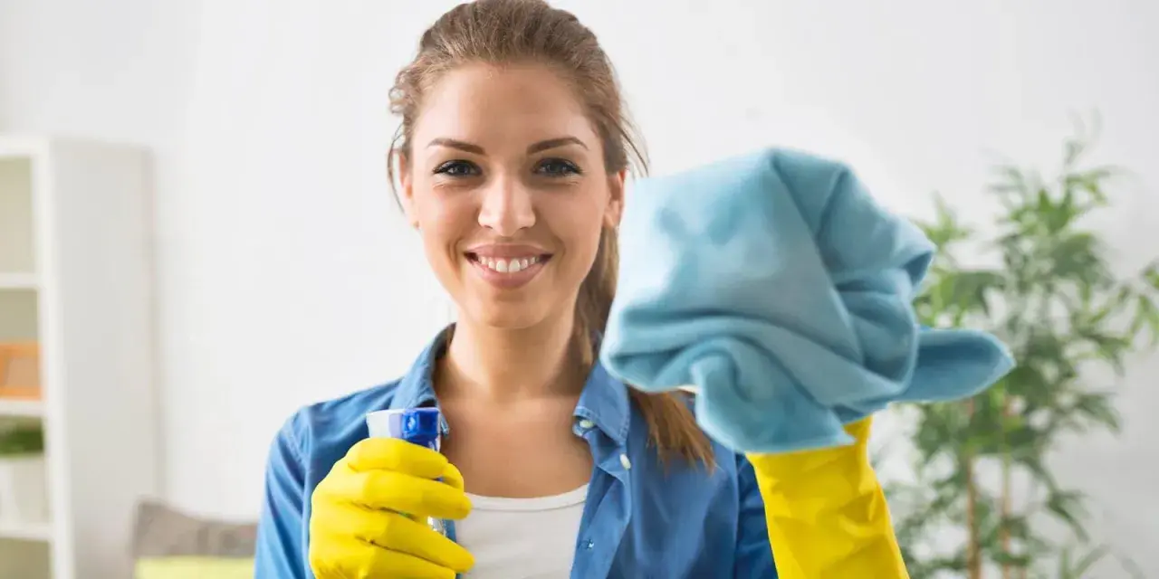 Donna sorridente con guanti gialli e panno blu, pronta a pulire le vetrate scorrevoli.