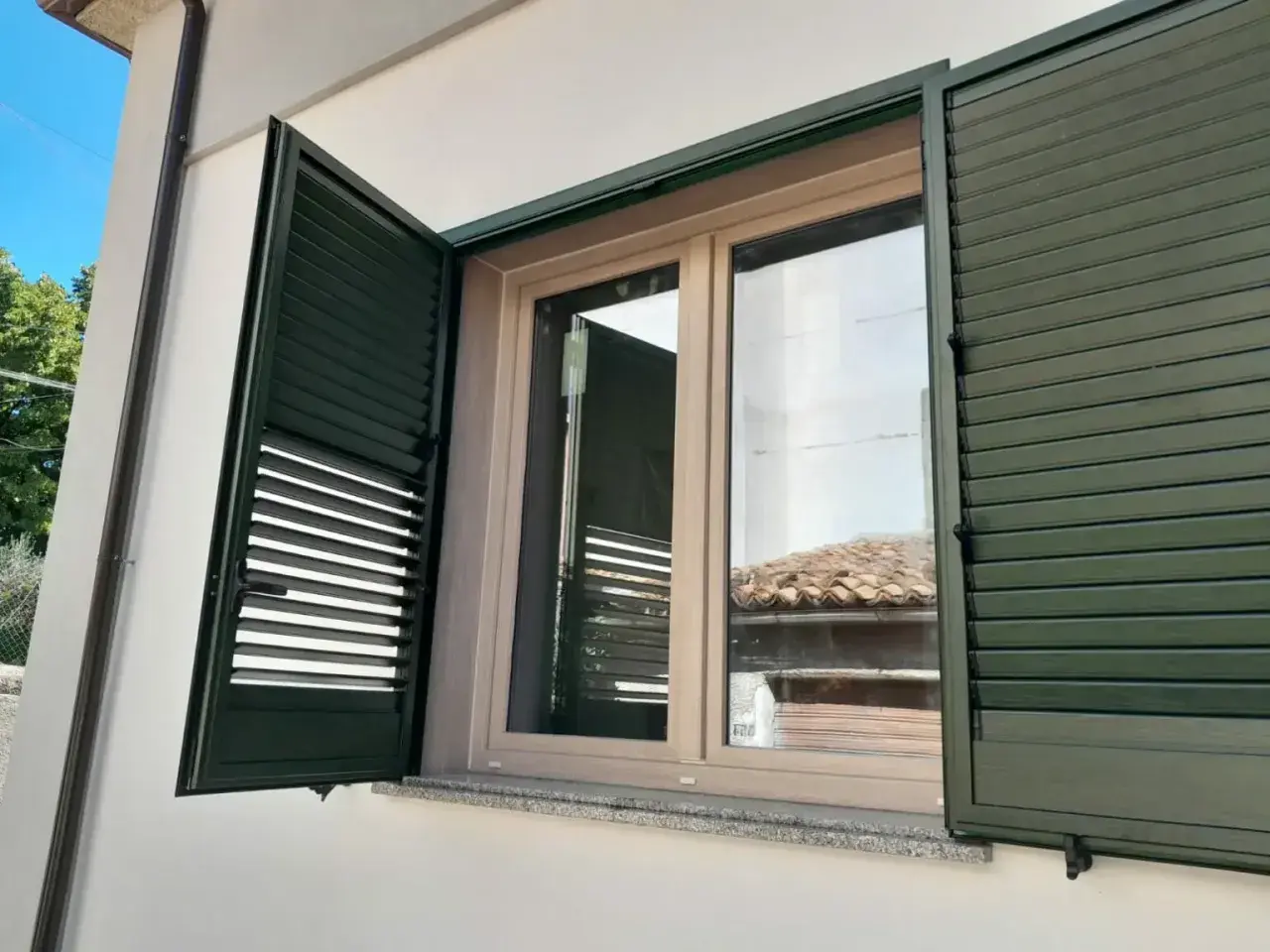 Infissi PVC effetto legno, colori naturali per un'estetica calda e moderna. Le persiane verdi si integrano perfettamente.
