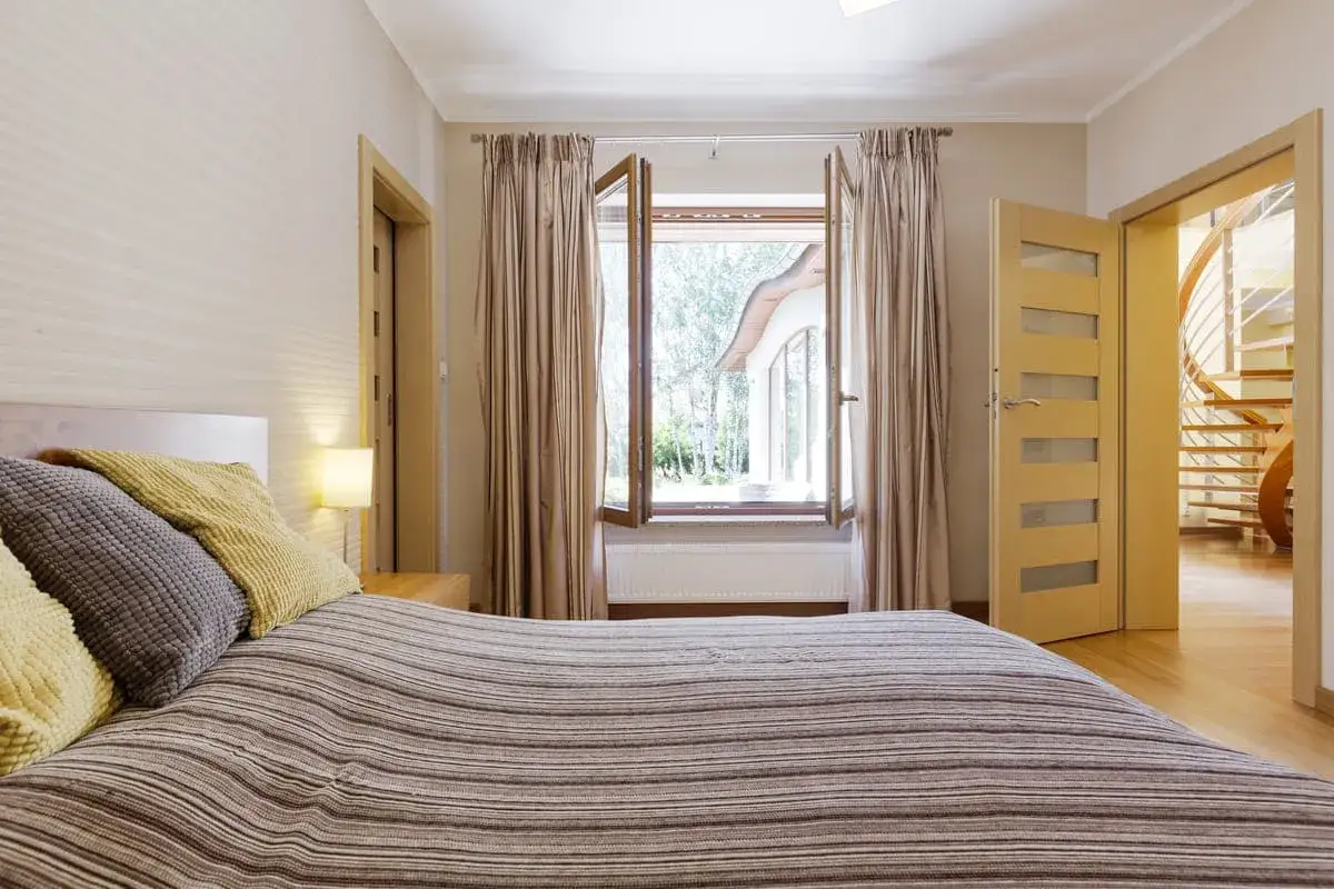 Letto a righe con cuscini, finestra aperta su un giardino lussureggiante e una scala a chiocciola visibile attraverso una porta. Forse è per questo che non aprire le finestre di notte.