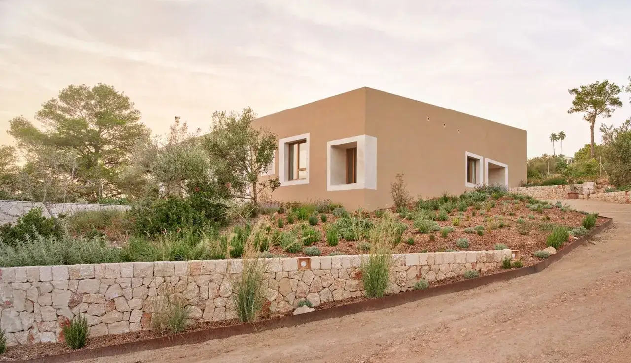 Casa moderna con architettura bioclimatica, immersa nel verde mediterraneo. Muri in pietra e ampie finestre incorniciate.