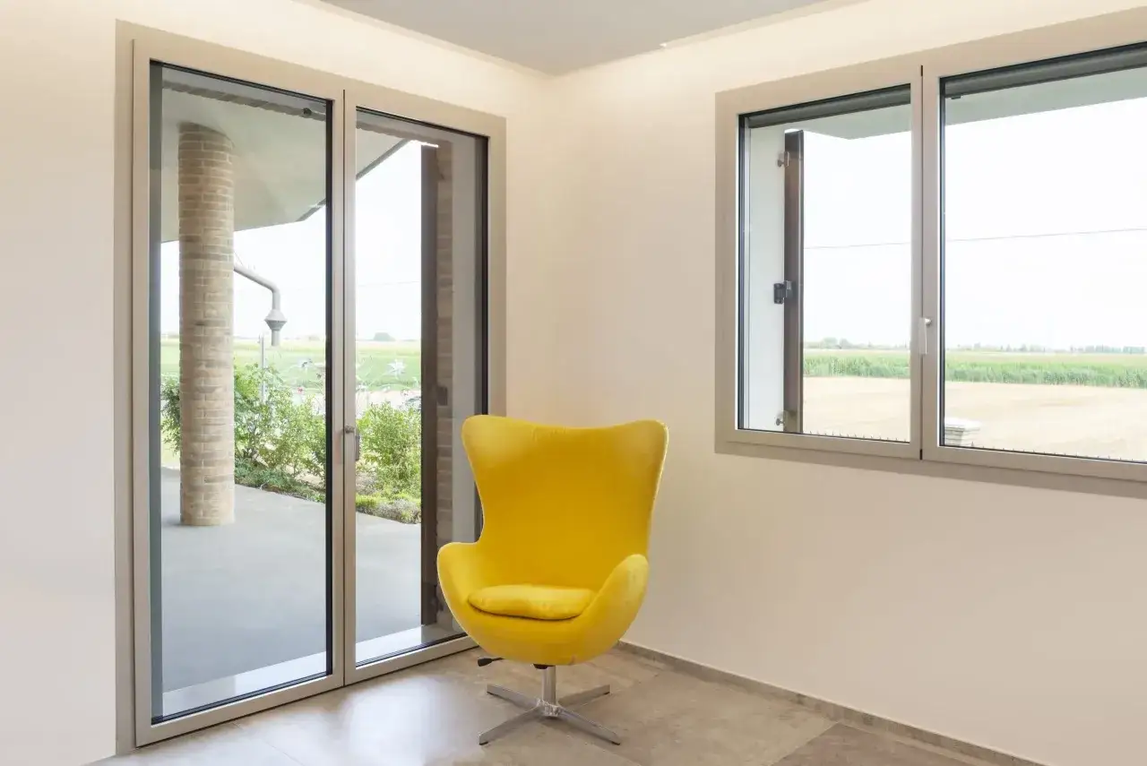 Poltrona gialla in un ambiente moderno con grandi finestre e porte in alluminio, che garantiscono resistenza e luminosit&agrave;.