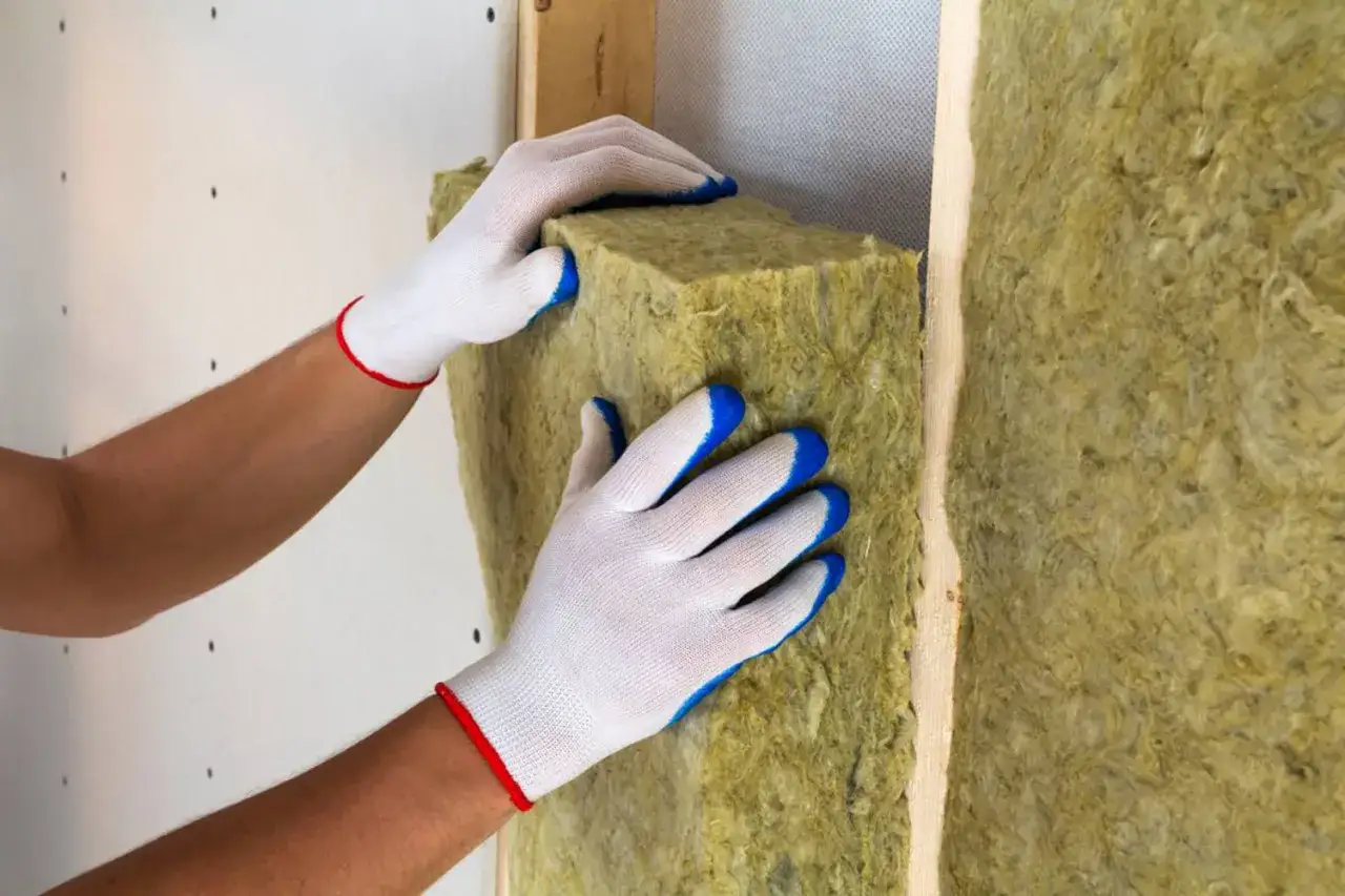 Mani guantate posizionano un pannello isolante per la coibentazione casa, migliorando l'efficienza energetica.