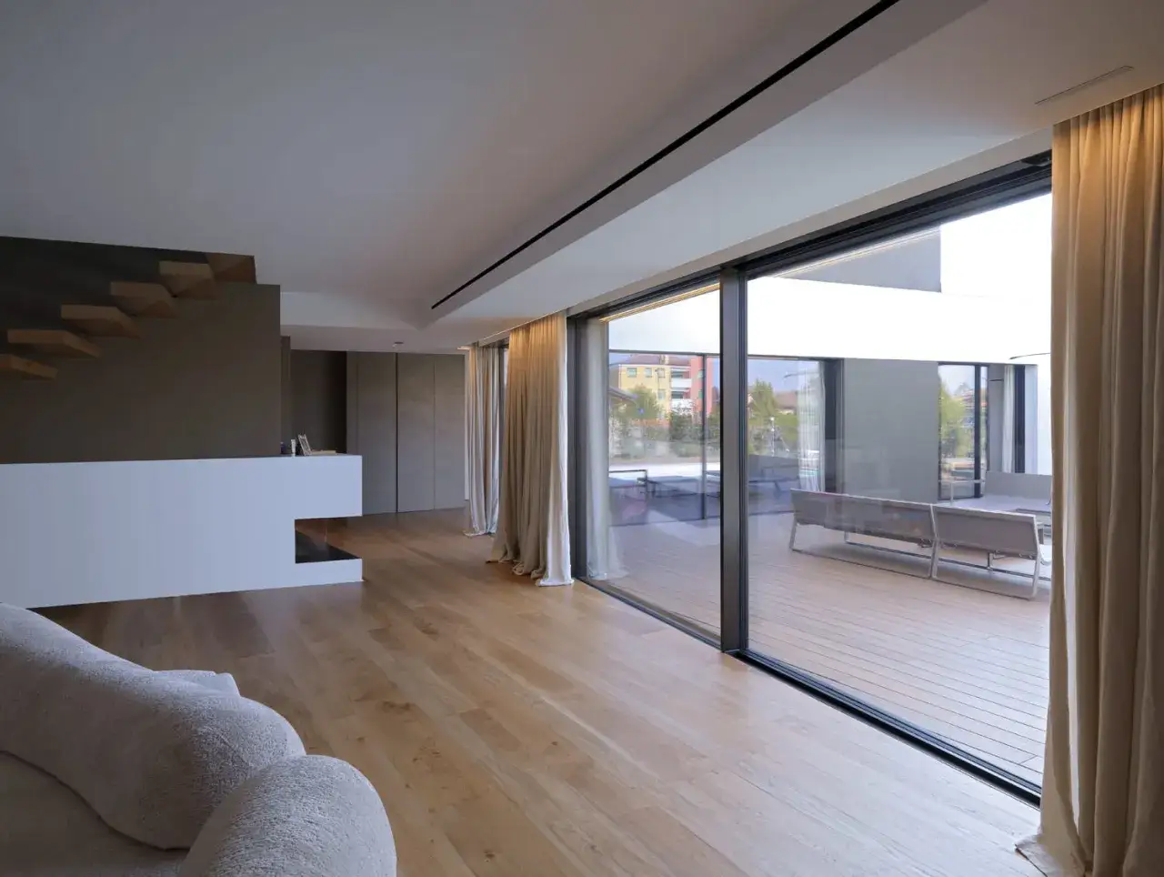 Interno moderno con parquet e un'ampia vetrata scorrevole che permette di allargare una finestra in condominio, affacciata su un patio con arredi da esterno.