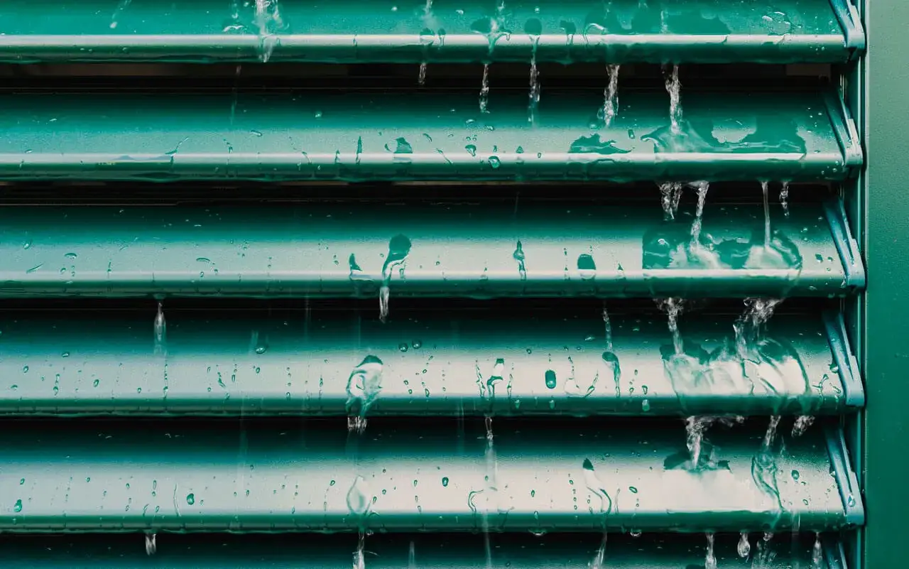 Acqua che scorre su persiane verdi in ferro. Un'immagine che suggerisce come pulire le persiane in ferro, mostrando la pioggia che lava via lo sporco.