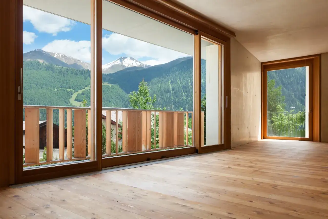 Interno moderno con pavimenti in legno e ampie vetrate che incorniciano montagne verdi. Strutture in alluminio legno per un design minimalista.