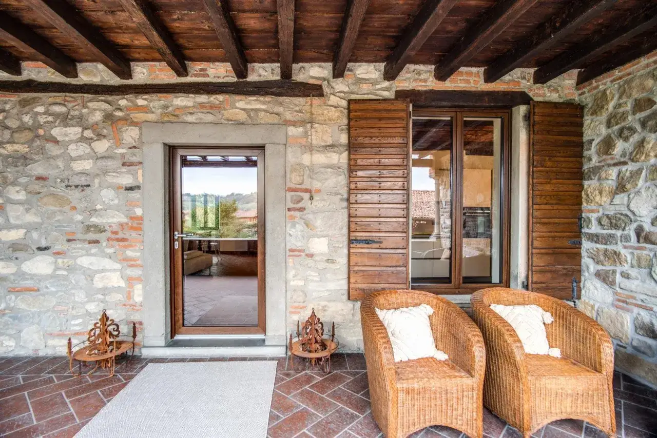 Portico in pietra con infissi per case di campagna, sedie in vimini e vista sul paesaggio.