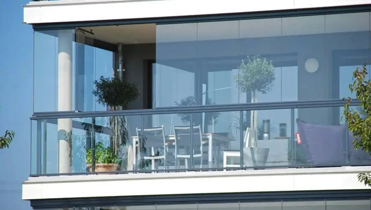 Balcone moderno con vetrata scorrevole per chiudere balcone con vetrata condominio. Tavolo, sedie e pouf viola.