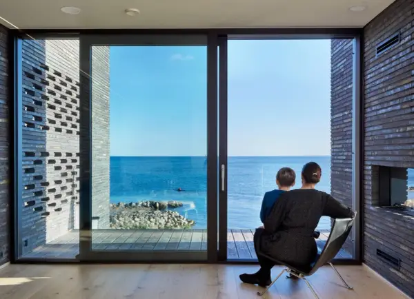 Madre e figlio osservano il mare da una stanza moderna, la luce naturale entra dalle ampie vetrate, illuminando l'ambiente.
